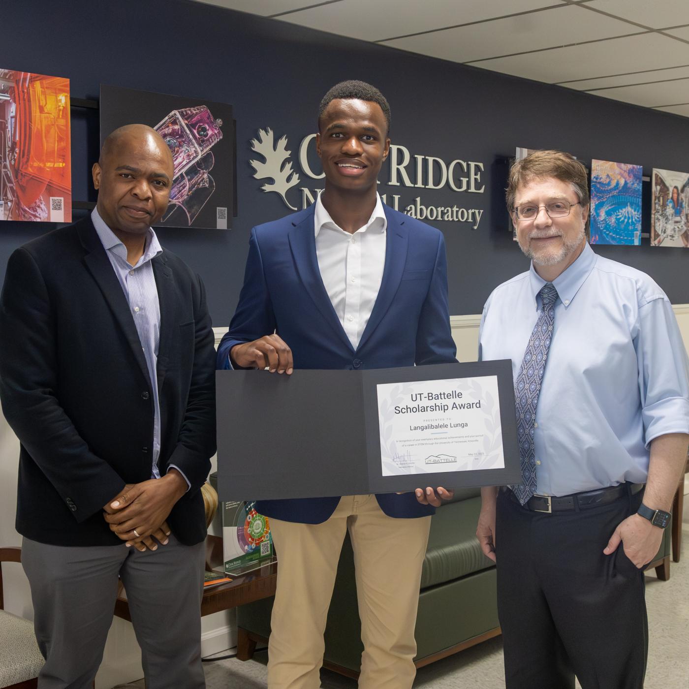 ORNL researcher Dalton Lunga and his son Langa Luna stand next to ORNL Director as he presents an award certificate to Langa (middle).