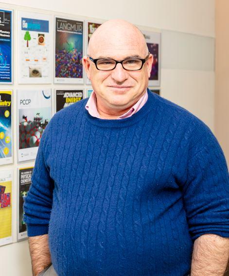 director of ORNL’s Chemical Sciences Division Rodger Rousseau is standing in front of a wall of magazine covers posing for a photo