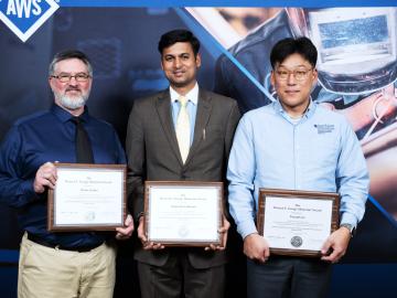 Three team members stand holding their award for bet paper by Welding Journal